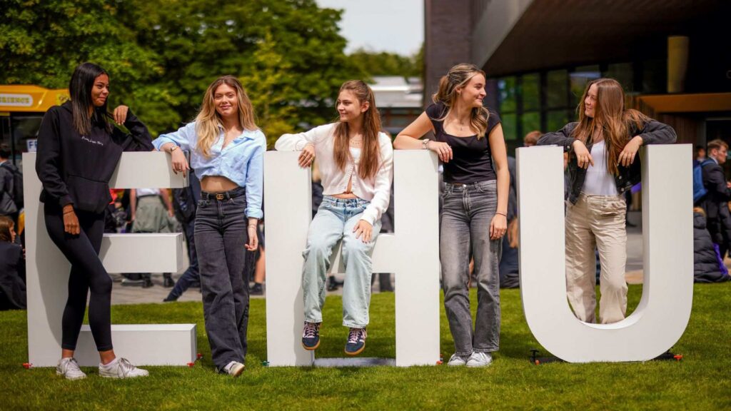 A group of students sit on or around giant letters EHU.