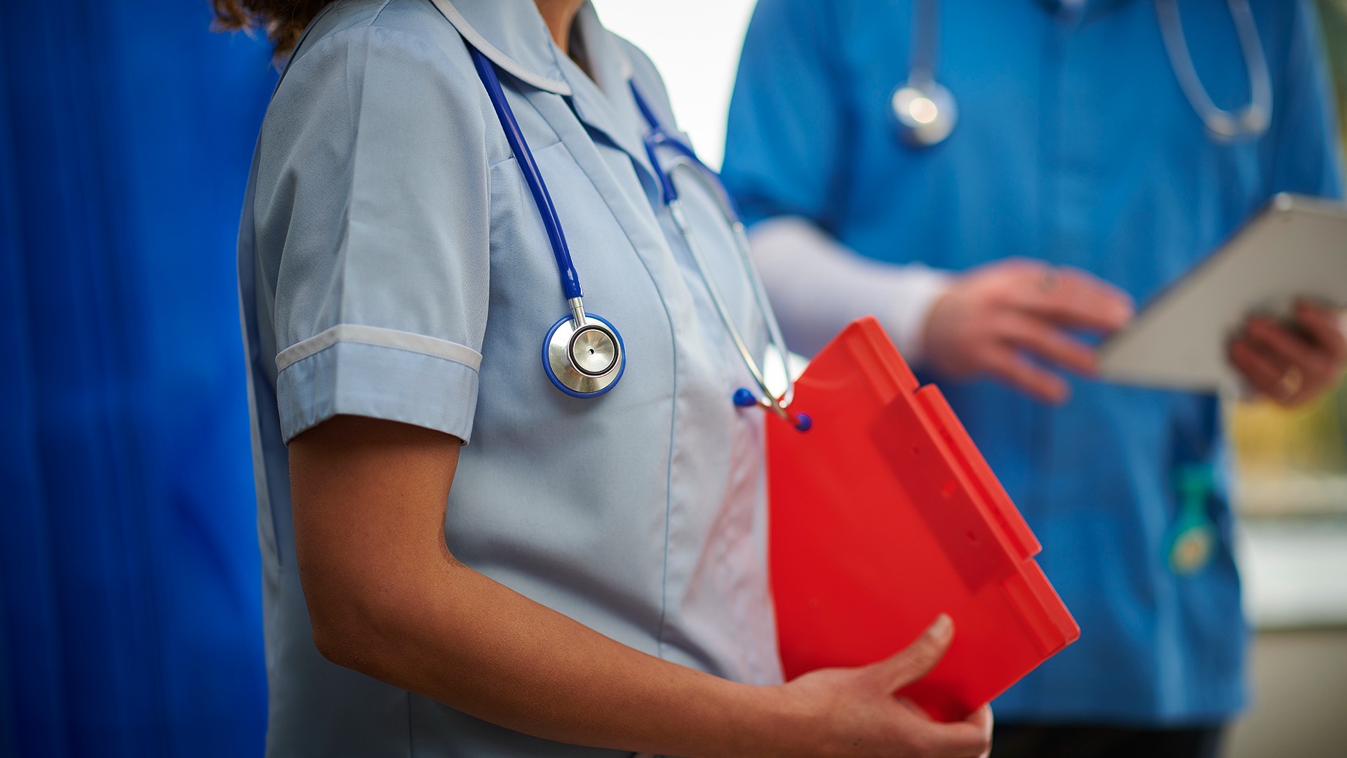 Close-up of a nurse holding a clipboard with a stethoscope around her neck.