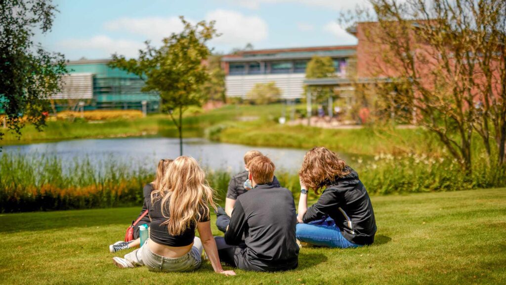 Students sitting at the edge of the lake on our green campus.